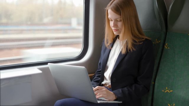 Young Beautiful Business Woman Goes by Train, Works on a Laptop and Looks at the Window