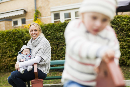 Happy mother with baby looking at son at playground