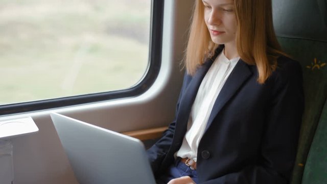 Young Blond Beautiful Business Woman with Straight Hair Goes by Train, Works on a Laptop