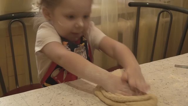 The girl on the kitchen table, knead the dough with your hands