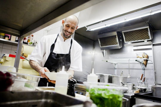 Happy chef holding dish at commercial kitchen