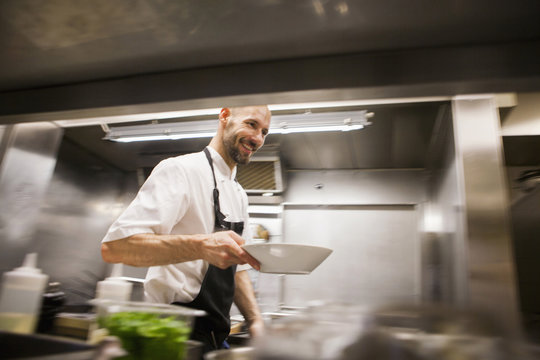 Happy chef holding dish while walking at commercial kitchen