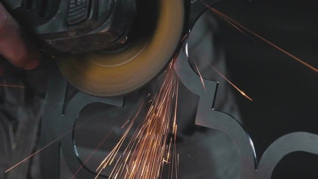 Decorative metalworking: the creation of an openwork decorative metal element. Sparks when cutting and grinding a metal product. Process of creating a decorative metal product: forged openwork metal.