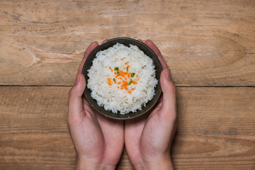 Close up of cooked rice in wooden in bowl holding by hands on wooden table