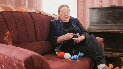 Senior lady sitting on the sofa and knits colourful wool - pensioners hobby at home
