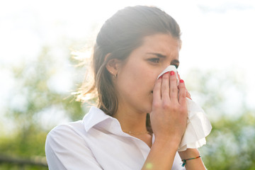 Sick woman blowing his nose into tissue, outdoors - Powered by Adobe