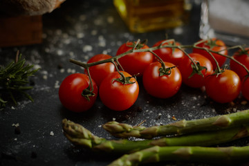 Cucina mediterranea, pomodorini, olio, sale, asparagi su fondo lavagna