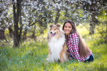 young beautiful woman with long hair sits on the lawn with collie dog. Outdoors in the park.