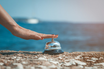 Close up of female hand ringing service bell against the ocean background. Summertime concept. - obrazy, fototapety, plakaty