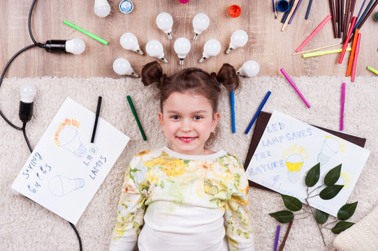 A little girl is lying among the markers and drawings of LED light bulbs