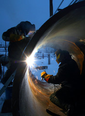 Two workers are welding inside and outside of the pipe