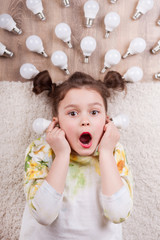 A little girl is lying among the markers and drawings of LED light bulbs