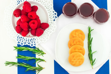 Fresh Red Raspberries on a white artistic plate / Red Fresh Raspberries on a white artistic plate with cookies, rosemary, chocolate and cream in the background.