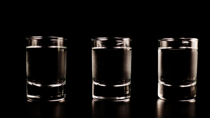 Three glasses, a shot of frozen vodka on a black table, on a black background