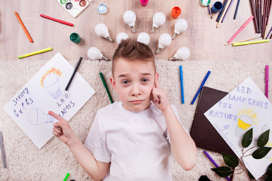 A little boy lies among the markers and drawings of LED bulbs
