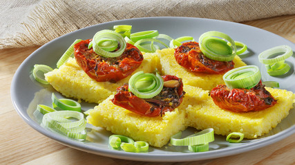 Pieces Corn polenta baked with cherry tomatoes, Parmesan cheese on the plate. 
