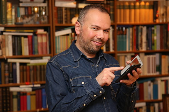Mann mit Smartphone vor B&uuml;chern