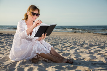 Woman sitting and reading book on beach