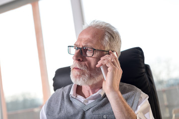 Portrait of bearded senior businessman talking on mobile phone, hard light