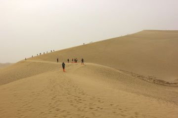 Fototapeta na wymiar Tourists climb the sand dunes , Dunhuang, Gansu province, China