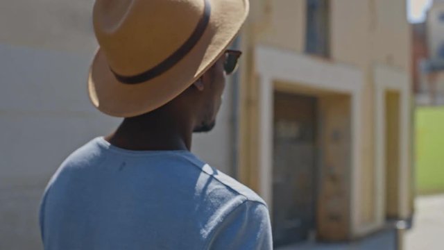 Handsome and trendy young black man walks by the camera while singing and mumbling a catchy tune, with sun shinning on his face, he acts like a hip hop gangster and shows an underground gesture