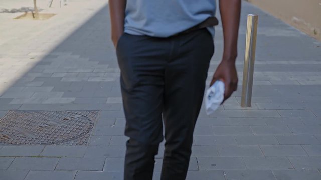 Young black hipster man slowly strolls through the city with a little package from the delivery post office he wears business outift of a startup enterpreneur. Handheld shot