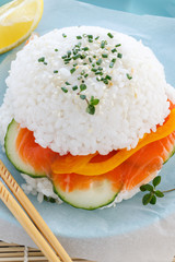 Sushi burger from rice, salmon, cucumber and pepper on a blue plate. Bright image of eating fast food.