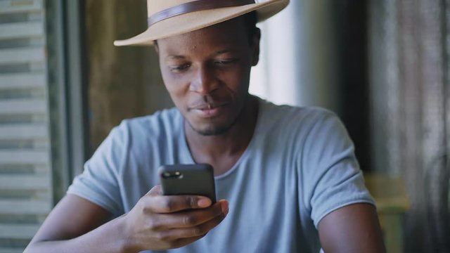 Handsome afro american man in a trendy and stylish outfit receives notifications on his phone, surprised and astonished by the news or prices on the online deals he is interested in.Handheld shot