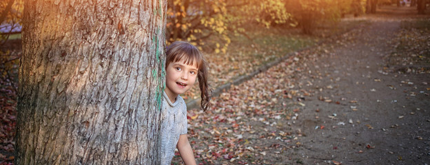 young girl hides behind a tree on a sunny day