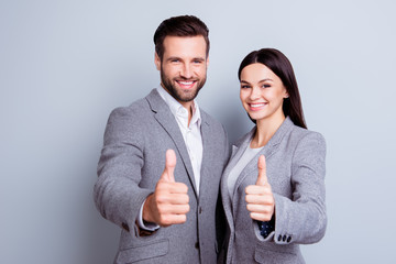 Two confident smiling businesspeople in formalwear showing thumbs-up on gray background