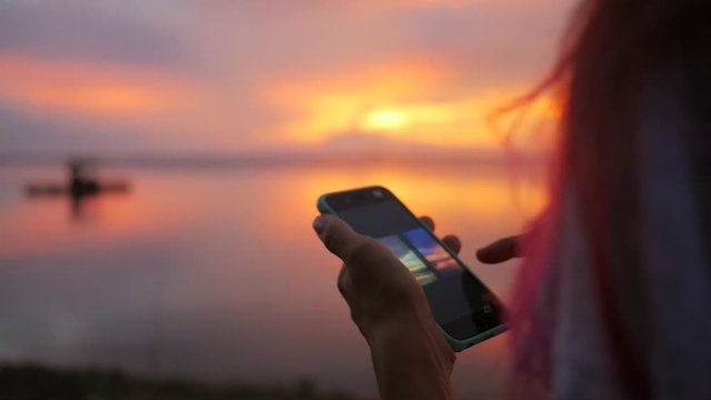 Young Hipster Girl Wathing Photos of Beautiful Sunset on Mobile Phone at Fisherman Pier. HD Slowmotion. Thailand.