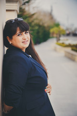 Happy smiling beautiful overweight young woman in dark blue jacket outdoors at the street. Confident fat young woman. Xxl woman, plus size woman.