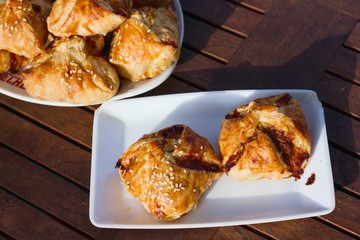 Homemade pasty with mince meat filling, sprinkled with sesame seeds and served on dark wood patio table on a sunny day