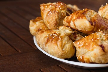 Homemade pasty with mince meat filling, sprinkled with sesame seeds and served on dark wood patio table on a sunny day