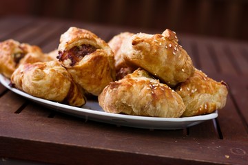 Homemade pasty with mince meat filling, sprinkled with sesame seeds and served on dark wood patio table on a sunny day