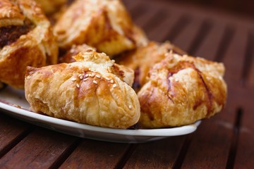 Homemade pasty with mince meat filling, sprinkled with sesame seeds and served on dark wood patio table on a sunny day