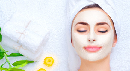 Spa woman applying facial mask. Closeup portrait of beautiful girl with a towel on her head applying facial clay mask