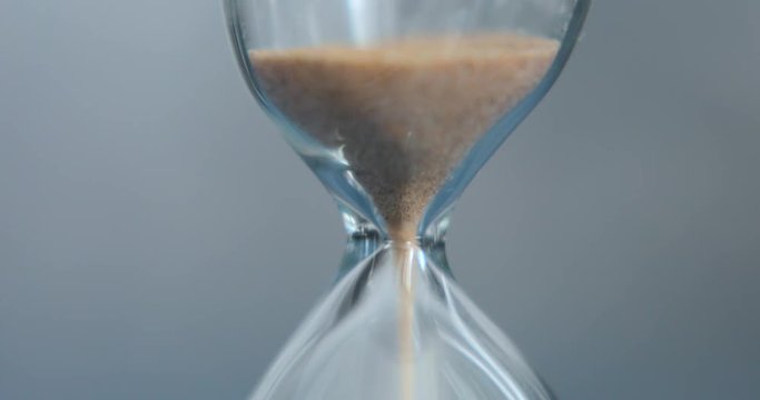 Hourglass on a gray background close-up. The sand of yellow color is poured into the lower part of the clock. In the center of the frame