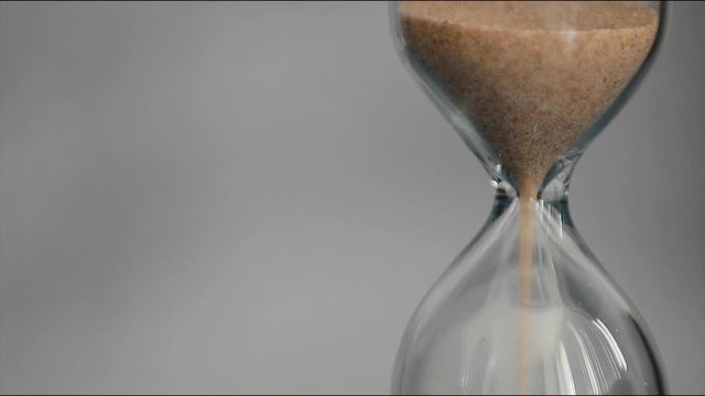Hourglass on a gray background. The sand of yellow color is poured into the lower part of the clock. In the right part of the frame