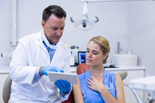 Dentist Discussing Over Digital Tablet With Female Patient