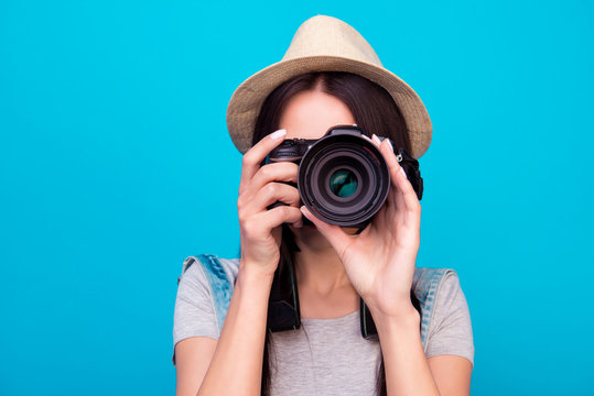 Close up photo of woman in hat on blue background taking a photo with digital camera