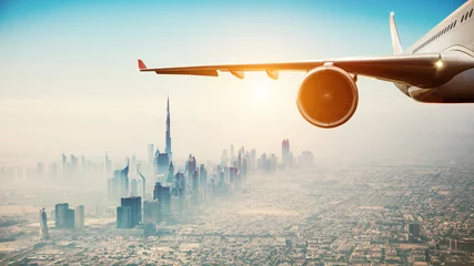 Tuinposter Dubai Close-up van commercieel vliegtuig dat over moderne stad vliegt