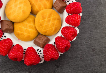Fresh Red Raspberries on a white artistic plate / Red Fresh Raspberries on a white artistic plate with cookies, rosemary, chocolate and cream in the background.