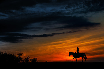A silhouette of a woman riding a horse at sunset