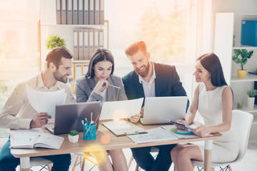 Happy smiling businesspeople analyzing the results of their work sharing opinions to each other in modern sunny office wearing formal wear