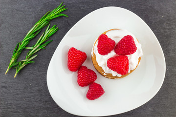 Fresh Red Raspberries on a white artistic plate / Red Fresh Raspberries on a white artistic plate with cookies, rosemary, chocolate and cream in the background.