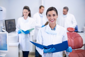 Smiling dentist holding file at dental clinic - Powered by Adobe