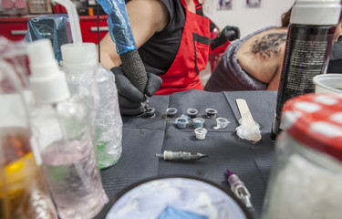Woman tattoo artist refilling pen from ink poured into small cups