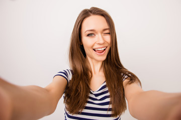 Young cheerful girl in striped t-shirt taking selfie and winking at camera against white background