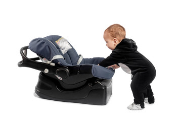 Smiling infant baby child standing near a car seat, isolated on white